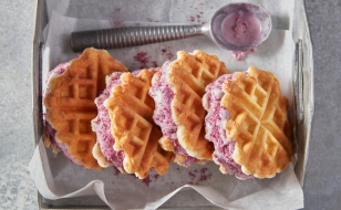 Four waffled biscuit ice cream sandwiches on parchment paper and silver serving tray with ice cream scoop.