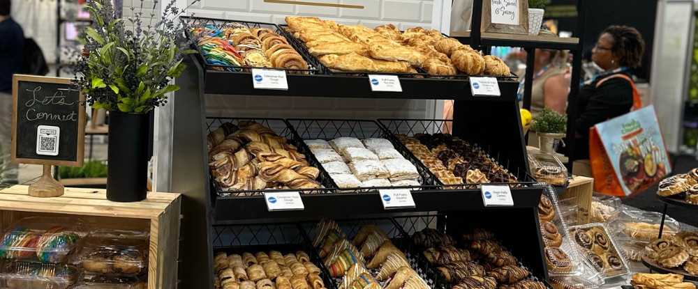 A bakery-case display at IDDBA showcasing fresh-baked pastries like croissants and cinnamon rolls.