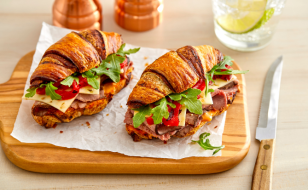 Croissant sandwiches stuffed with spicy roast beef, cheese, and vegetables sitting on parchment paper on top of a cutting board